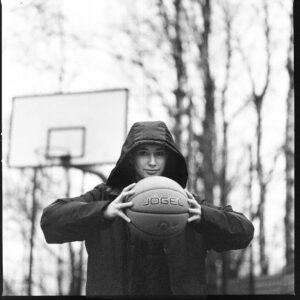 Black and white image of person holding basketball outdoors in winter.