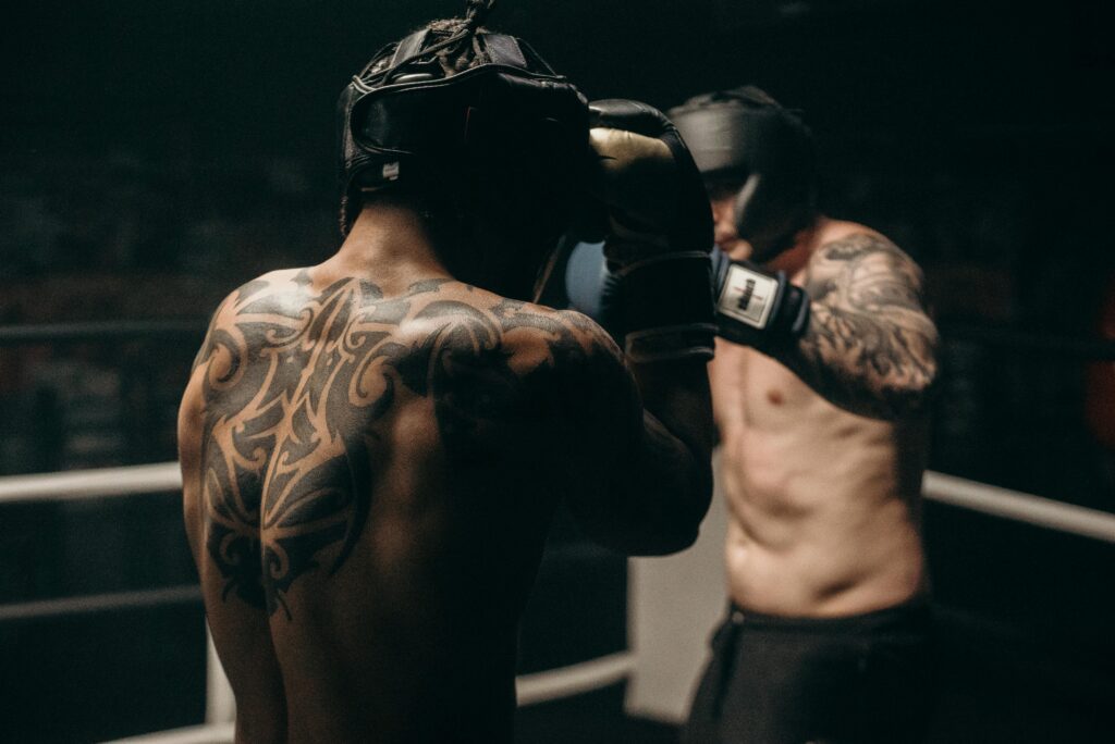 Two tattooed boxers sparring in a dimly lit gym, showcasing strength and skill.