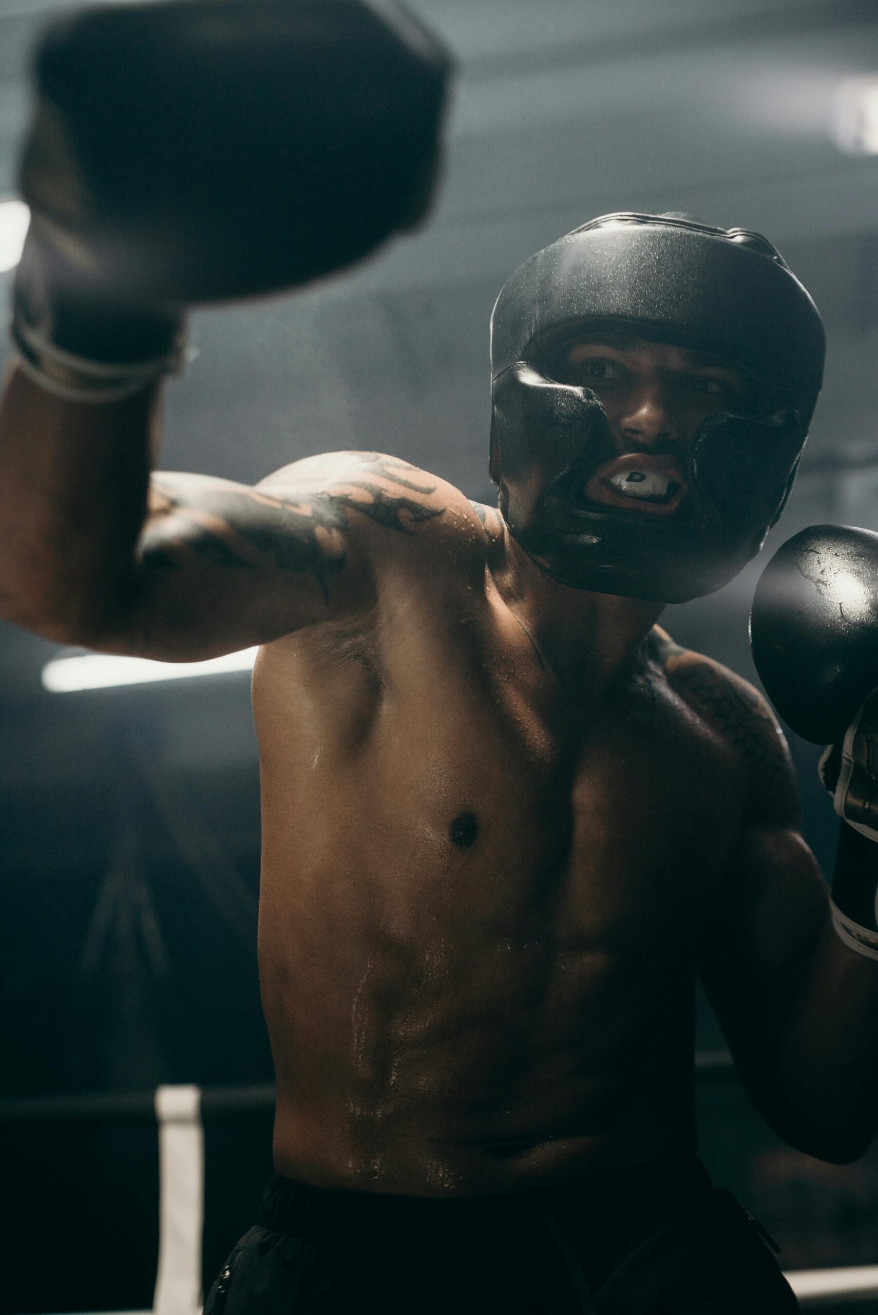 A muscular boxer practicing punches indoors with protective gear in a gym.